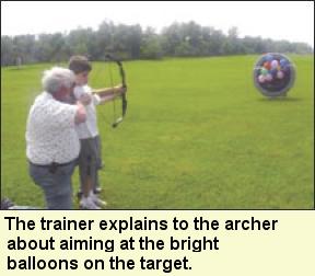 The trainer explains to the archer about aiming at the bright balloons on the target. Photo submitted by Camp Abilities.