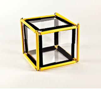 Photo shows a square prism (cube) constructed from Geometro tiles with the corresponding rod model placed over it, in 3-D, in Position 1. That is, slightly rotated counter-clockwise from the starting, face-on position (viewed from the left).