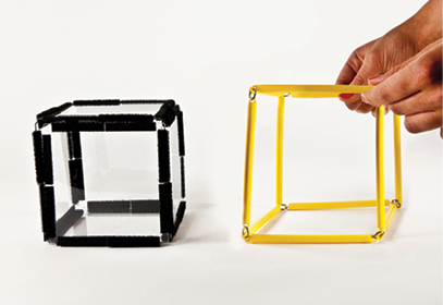 Photo shows a square prism (cube) constructed from Geometro tiles, in 3-D, standing beside the corresponding rod model being held in 3-D.