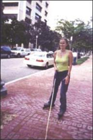 Stacy skates along a sidewalk using her cane.