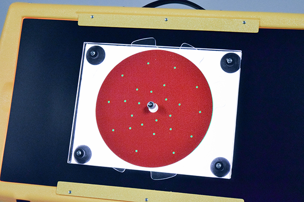 Photograph of the APH Light Box set up for use with the rectangular blackout sheet from the Level 1 Light Box Materials, the APH Plexiglas® Spinner, and a red sparkle overlay with perforations to let light shine through.