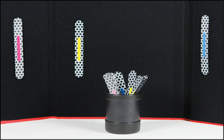 A black felt tri-fold board with three Phase II Advanced MATCH STICKS attached: one pink-, one yellow-, and one blue-striped stick. A black plastic cylindrical cup in front of the board holds several more Phase II Advanced MATCH STICKS.