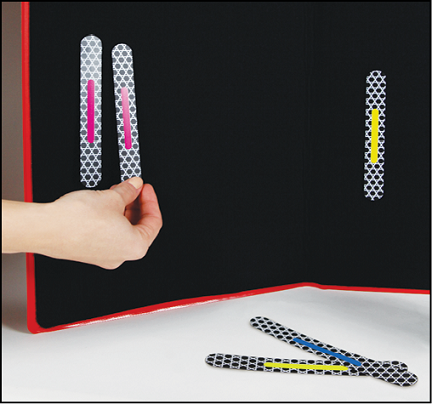 A black felt tri-fold board with two Phase II Advanced MATCH STICKS	 attached: one pink- and one yellow-striped stick. A hand attaches a pink-striped MATCH STICK next to the attached pink-striped MATCH STICK. Two other Phase II Advanced MATCH STICKS lie on a white surface in front of the board.
