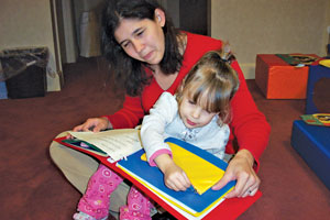 A two-year-old explores a real object illustration in a tactile book, unzipping a small purse attached to the book's page.
