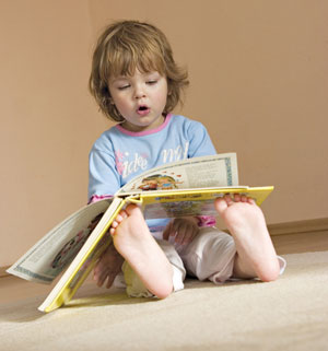 A young child independently turns pages of a picture book as she pretends to read aloud.