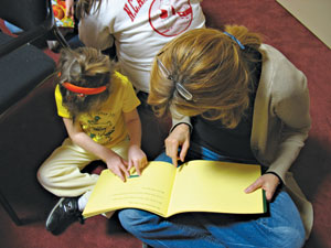 A preschooler examines a tactile illustration in a book she shares with a caregiver.