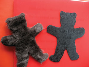 Fake fur fabric, cut in the shape of a child's teddy bear, glued to a paper page.