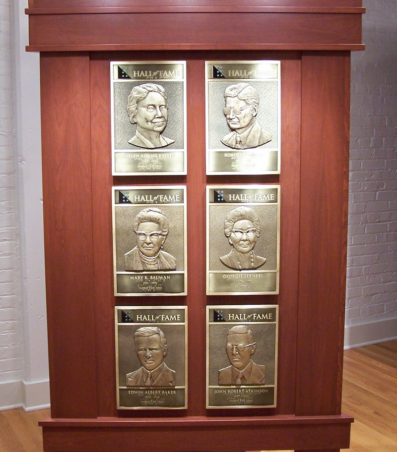 A close-up view of one face of a kiosk. The displayed plaques are: Helen Keller, Robert Irwin, Mary K. Bauman, Georgie Lee Abel, Edwin Baker, and Robert Atkinson