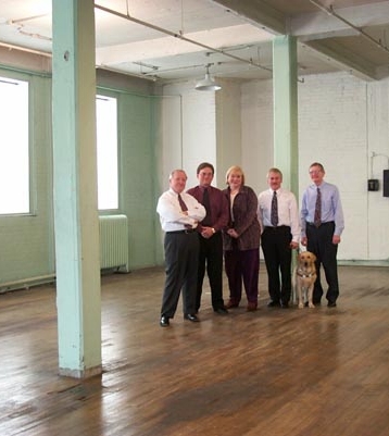 APH employees stand in the future Hall of Fame prior to renovation: the room has a wood floor, tall columns, and large windows.