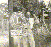 James Max Woolly standing next to a Lion's Club road sign