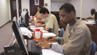 Men sitting at a row of computers, transcribing braille