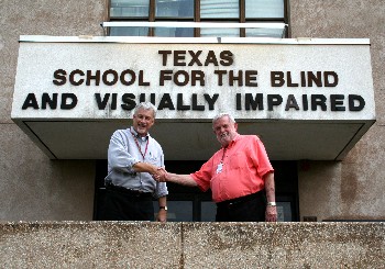 Bill Daugherty and Phil Hatlen shaking hands in front of a Texas School for the Blind and Visually Impaired marquee