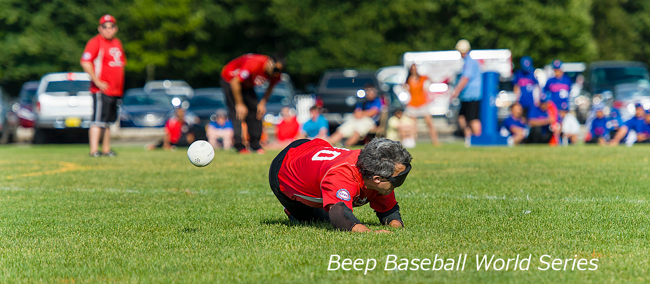 Beep baseball player dives to the ground, just missing the baseball.