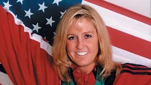 Zorn-Hudson wearing a red track suit with the United States flag held above her shoulders. Medal ribbons can be seen around her neck.