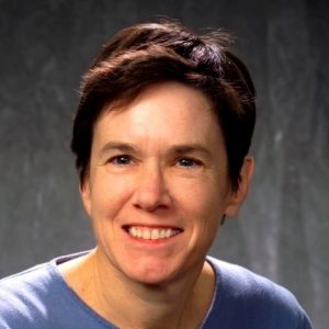 Color, head-and-shoulders photo of Jane Erin. She is looking at the camera with a broad smile. She wears a light blue shirt and has short, dark brown hair.